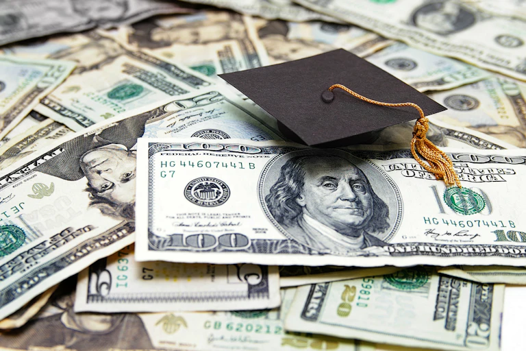 A graduation cap sits atop a pile of U.S. currency.