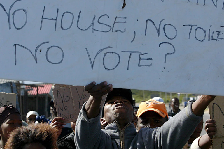 A group of people holding placards. One reads "No house, no toilets, no vote?"