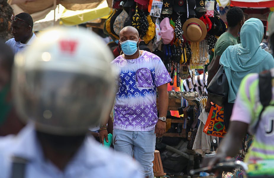 Man wearing mask, walking among other people with market stall in background