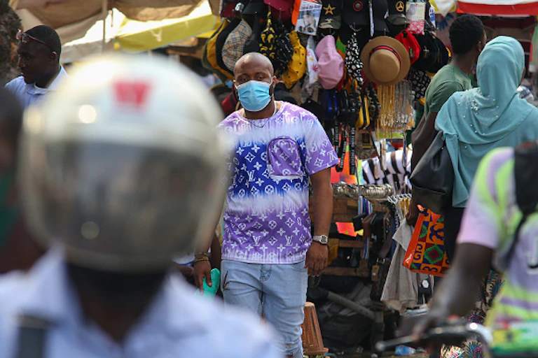 Man wearing mask, walking among other people with market stall in background