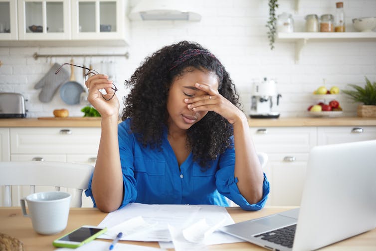 Tired young African American single mother feeling stressed because of financial problems, working through finances in kitchen late at night, doesn't have enough money to pay off mortage debt