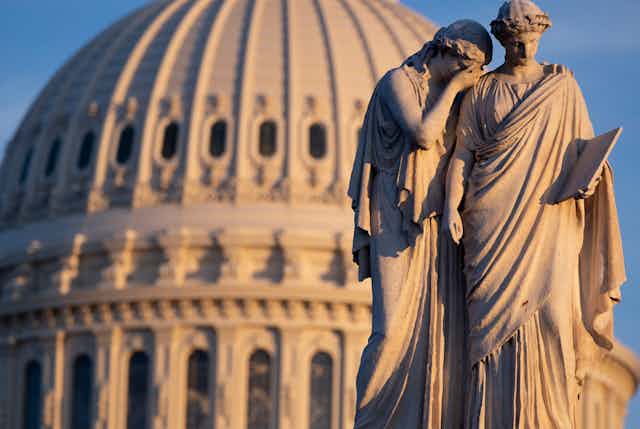 Classical statue of two figures against the backdrop of the US Capitol Building, Washington.
