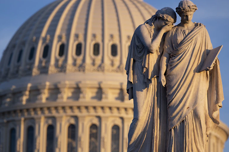 Classical statue of two figures against the backdrop of the US Capitol Building, Washington.