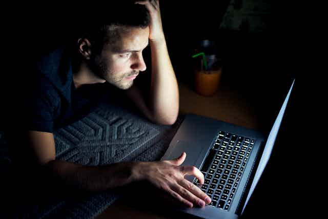 Man in dark room uses laptop lying on floor