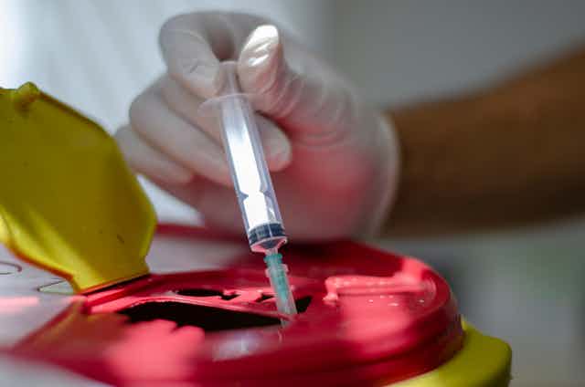 Hand with surgical glove puts syringe in waste box