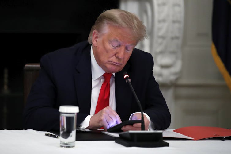 Donald Trump types on his mobile phone while sitting next to a glass of water