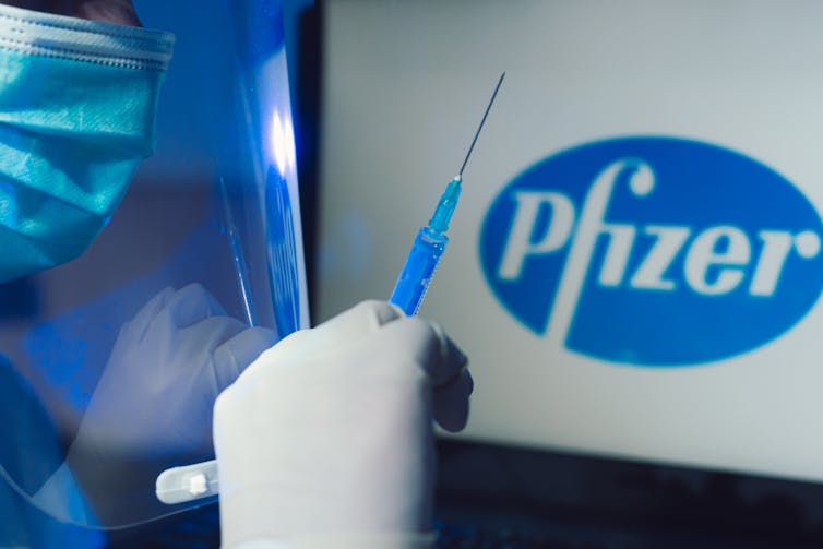 Medical gloved hand holds syringe in front of Pfizer logo