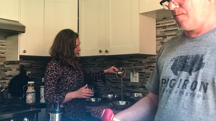 A couple in a kitchen makes music with kitchen objects.