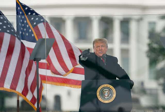 President Trump behind the podium points at the crowd with two American flags behind him