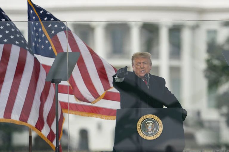 President Trump behind the podium points at the crowd with two American flags behind him