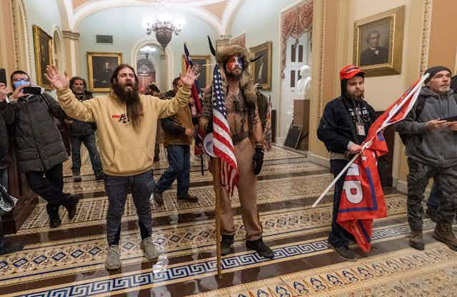 Three pro-Trump rioters, one wearing an employee ID badge around his neck, are seen outside the Senate Chamber inside the Capitol on Jan. 6.