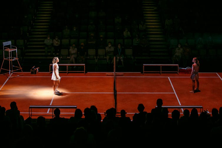 The audience on two sides of a red tennis court as a stage.