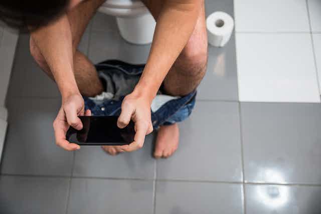 A man sitting on the toilet using his phone