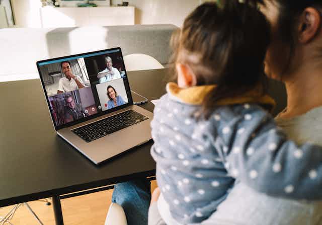 Woman holding baby in video conference on laptop with four people
