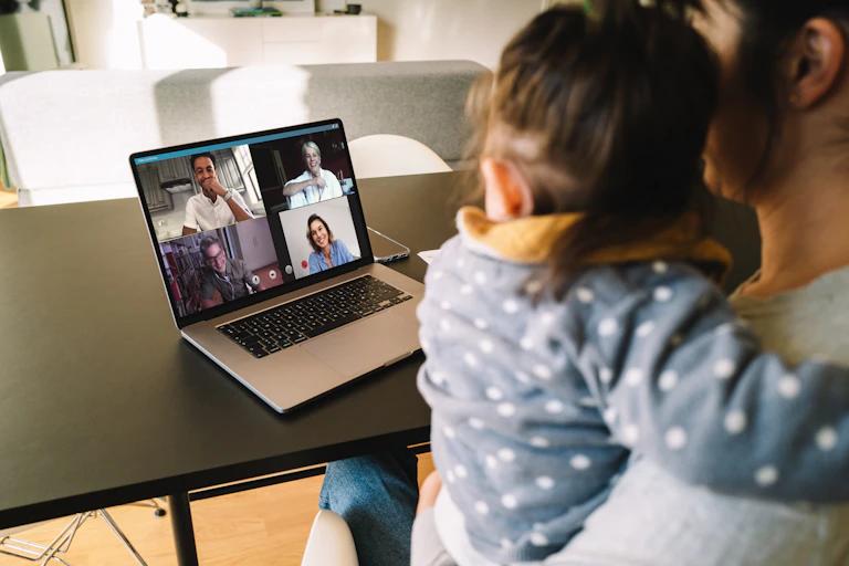Woman holding baby in video conference on laptop with four people
