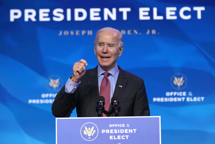 Joe Biden giving a speech under a sign that says 'President Elect.'