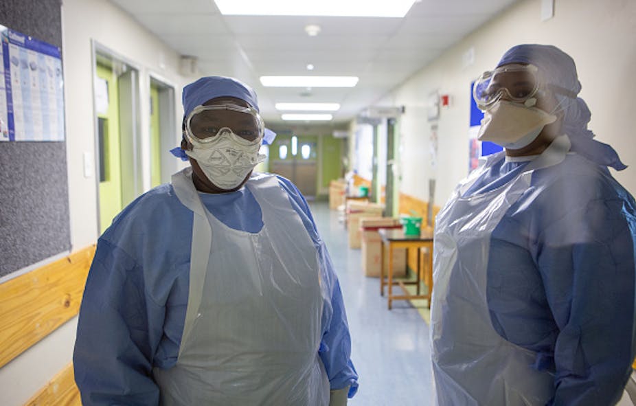 Two people wearing protective gowns and masks stand in a hospital corridor