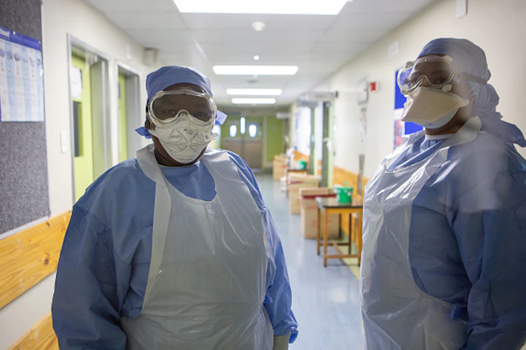 Two people wearing protective gowns and masks stand in a hospital corridor