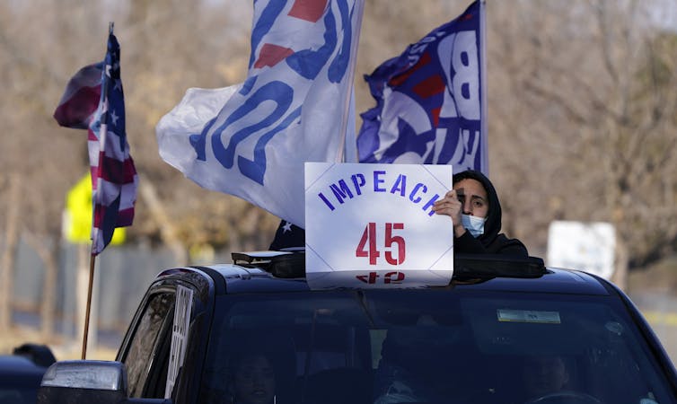 A man holds up a placard calling for Trump's impeachment through the sun roof of a car.