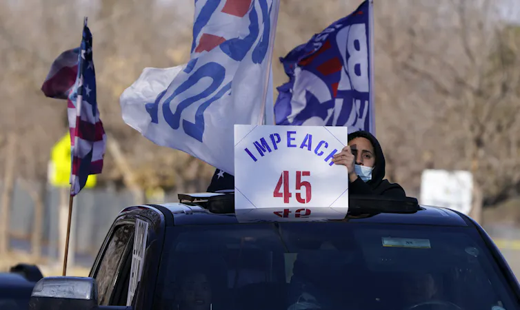 A man holds up a placard calling for Trump's impeachment through the sun roof of a car.