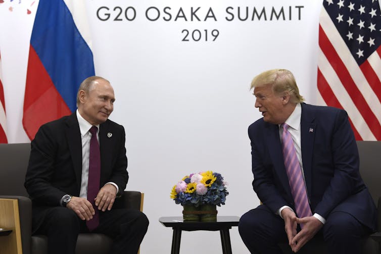 Trump chats with Putin with U.S. and Russian flags behind them.