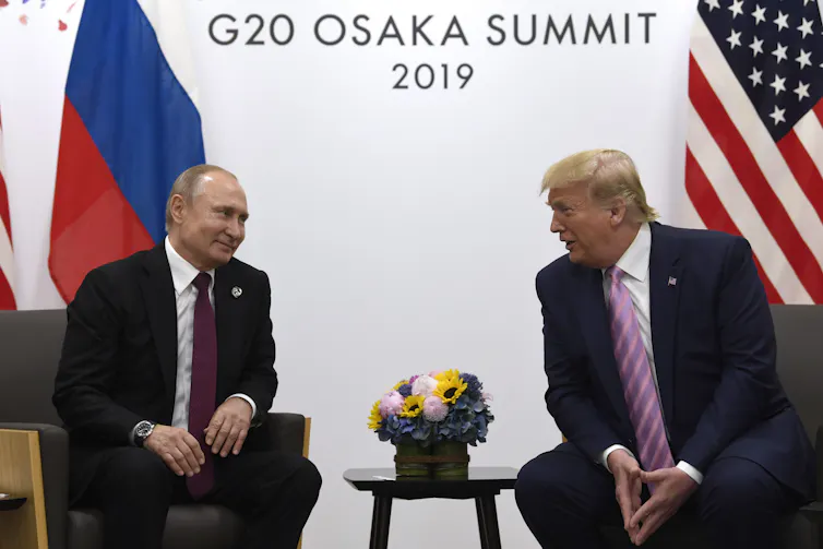 Trump chats with Putin with U.S. and Russian flags behind them.