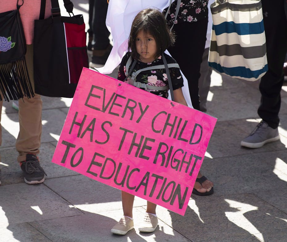 A young girl holds a sign during a protest. The sign reads: every child has the right to education.