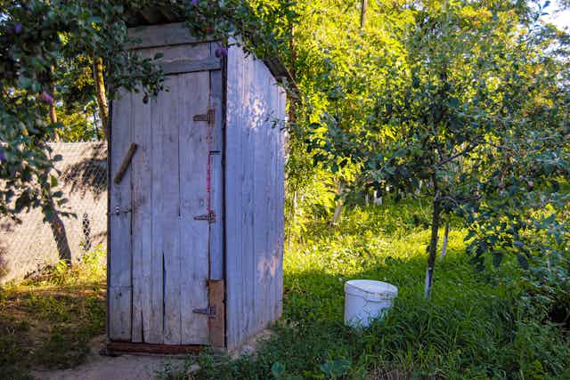 An wooden outhouse with a bucket beside it