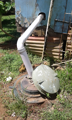 A white pipe juts out of a blue plastic tank and into the ground.
