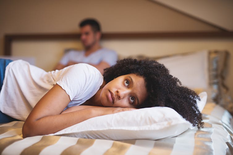 Sad woman lying on bed facing away from her partner