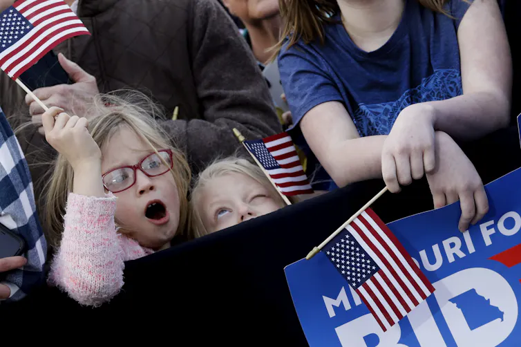 Children, one wearing red eyeglasses, wave U.S. flags.