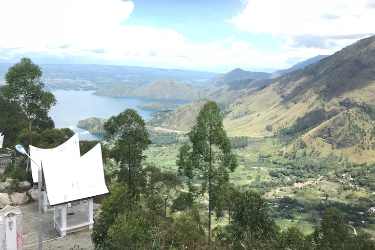 Aerial view of Urat village, with mountains in the backdrop and 2 indigenous houses painted white.
