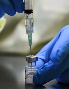 Gloved hands filling a syringe from a vial