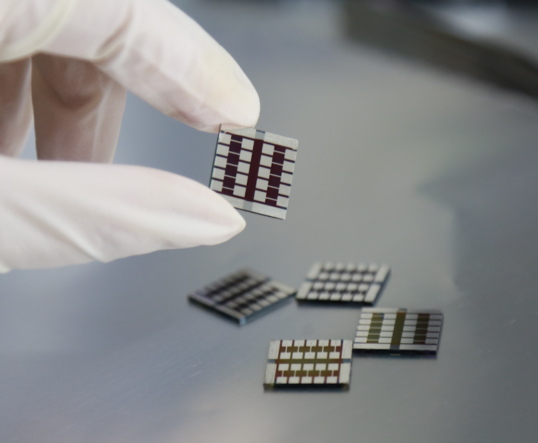 A gloved hand holds up a small solar cell.