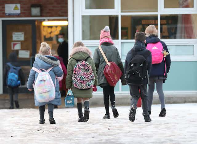 Five children wearing backpacks enter a school.
