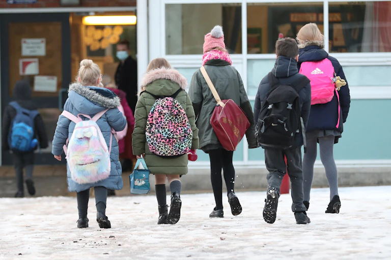 Five children wearing backpacks enter a school.