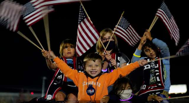 Children wave American flags at a night-time event.