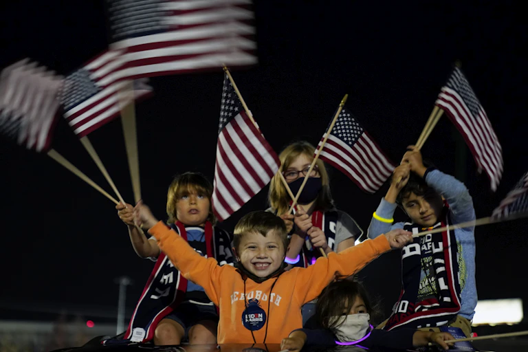Children wave American flags at a night-time event.