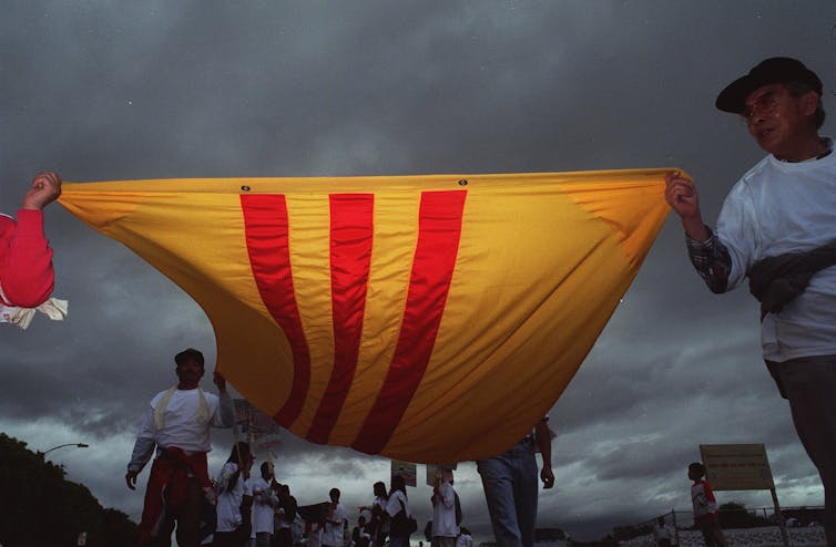 Four people carry the South Vietnam flag under cloudy skies