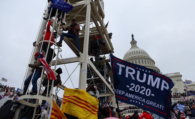 Rioters scale structures while flying flags outside the Capitol.