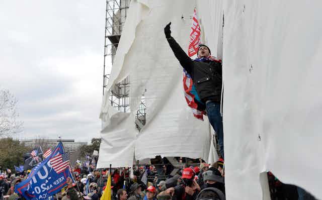 A man hanging from scaffolding raises his middle finger.