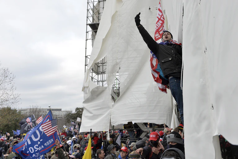 A man hanging from scaffolding raises his middle finger.