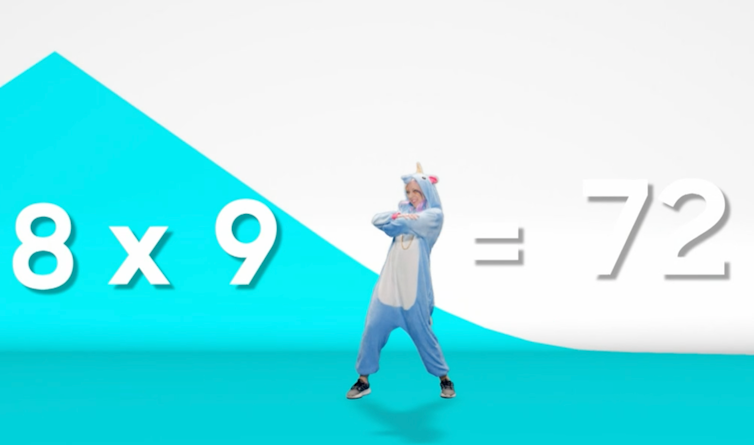 A woman in a unicorn onesie dancing while teaching maths.
