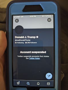 A hand is seen holding a phone showing Donald Trump's suspended Twitter account.