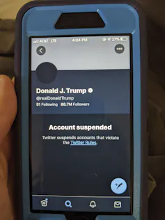 A hand is seen holding a phone showing Donald Trump's suspended Twitter account.