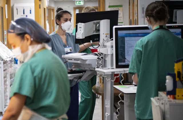 Three nurses on a hospital ward wearing PPE. 