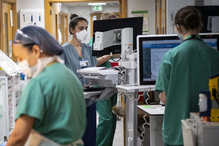 Three nurses on a hospital ward wearing PPE.