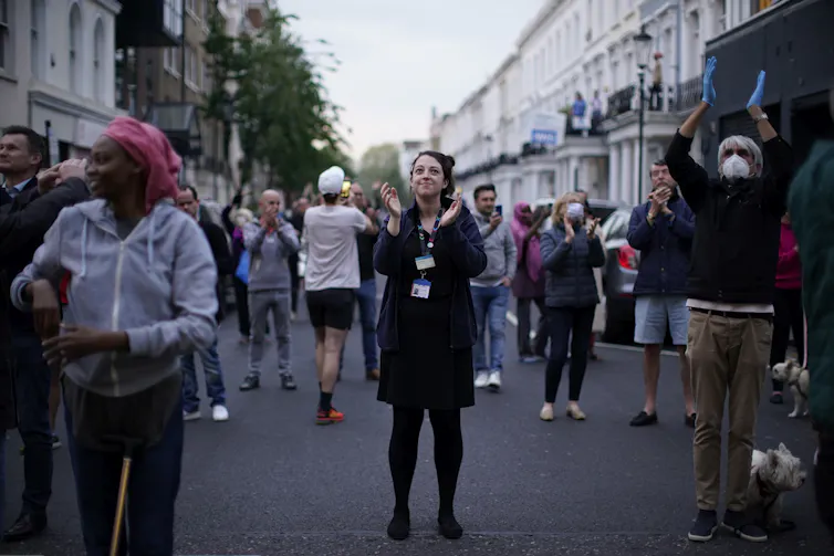People stand in a London street and applaud.