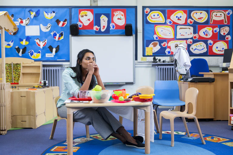 Tired childcare sitting in empty classroom.