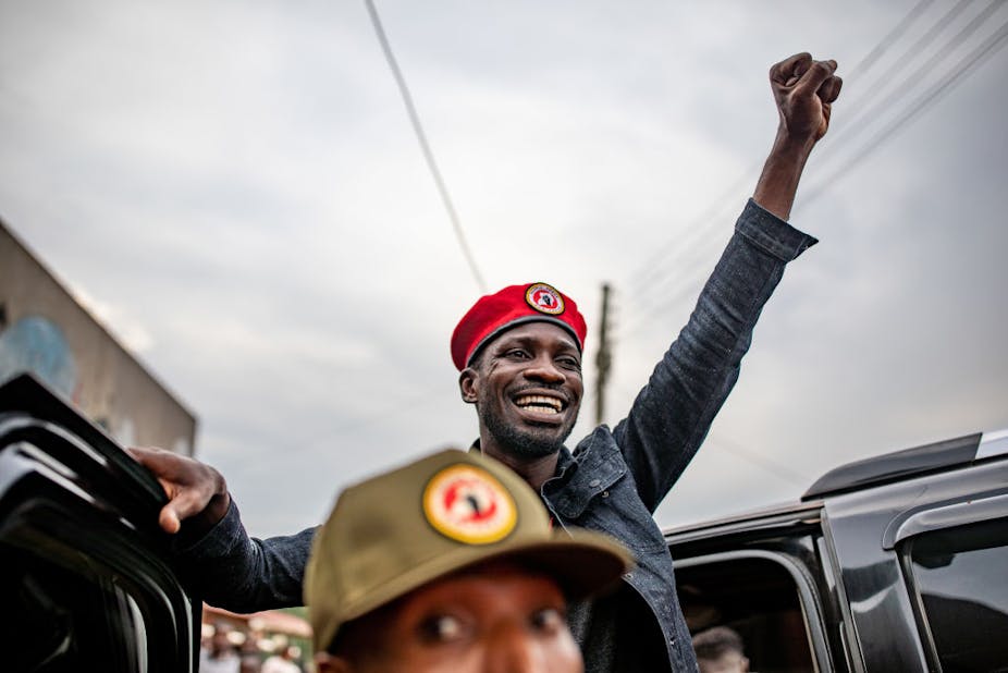 Robert Kyagulanyi Ssentamu. smiling and wearing a red beret, raises his fist in the air